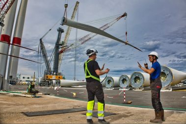 Deux hommes en charge de l'embarquement des pâles se coordonnent pour guider les engins de levage