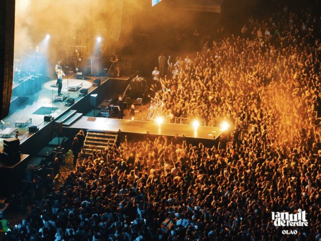 Les éclairages oranges de cette photo prise par drone lors d'un festival, colorent la foule qui l'oppose à l'artiste dans une ambiance bleutée.