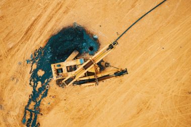 Photo prise lors d'une formation drone. Une foreuse en panne aux couleurs du TP se confond dans le décor couleur sable. Dans cette photo vue du ciel par drone, on distingue le trou du forage et la substance noire qui s'en découle.