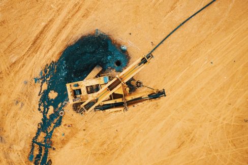 Photo prise lors d'une formation drone. Une foreuse en panne aux couleurs du TP se confond dans le décor couleur sable. Dans cette photo vue du ciel par drone, on distingue le trou du forage et la substance noire qui s'en découle.