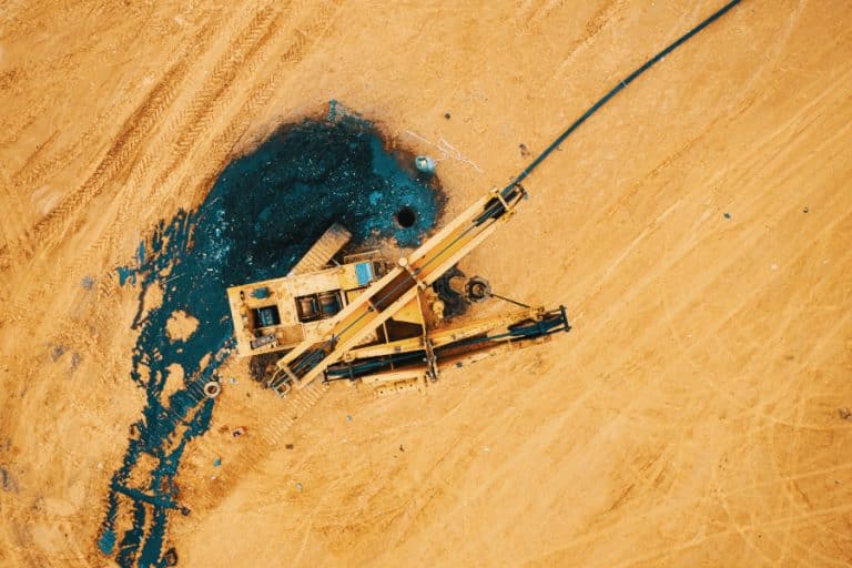 Photo prise lors d'une formation drone. Une foreuse en panne aux couleurs du TP se confond dans le décor couleur sable. Dans cette photo vue du ciel par drone, on distingue le trou du forage et la substance noire qui s'en découle.