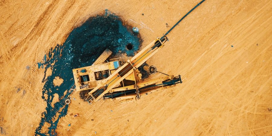Photo prise lors d'une formation drone. Une foreuse en panne aux couleurs du TP se confond dans le décor couleur sable. Dans cette photo vue du ciel par drone, on distingue le trou du forage et la substance noire qui s'en découle.