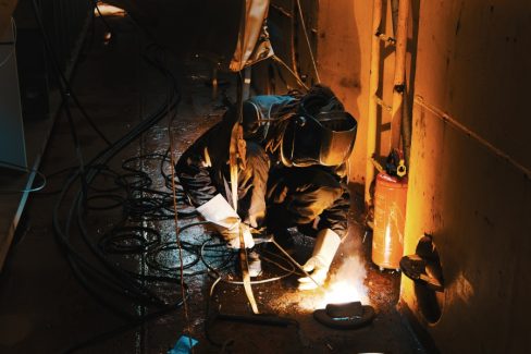 Un soudeur est en fond de cale afin d'améliorer et de renforcer un anneau de fixation. La photographie en milieu industriel un domaine d'excellence chez Olao