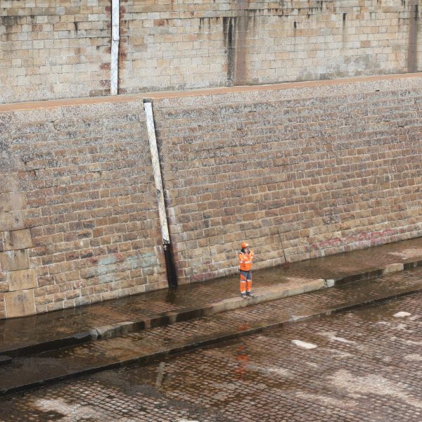 Bouygues-St Naz-Port-Greenov-Fev 241A0795 un ouvrier en tenue de chantier se tient seul au milieu d'une des formes Joubert sur le port de Saint Nazaire.