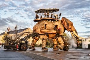 Le grand éléphant de Nantes se promène sur le parc des chantiers sous un soleil couchant