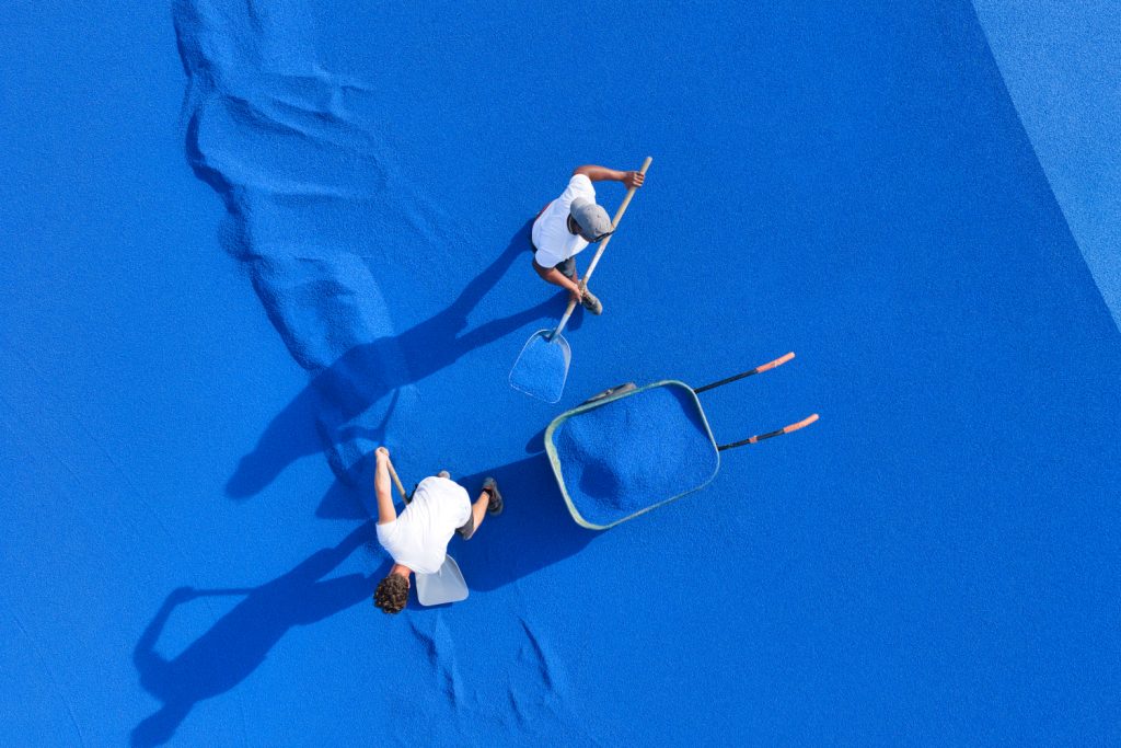Un compagnon de Sportingsols répand les granulats bleus à la pelle sur la piste d'athlétisme