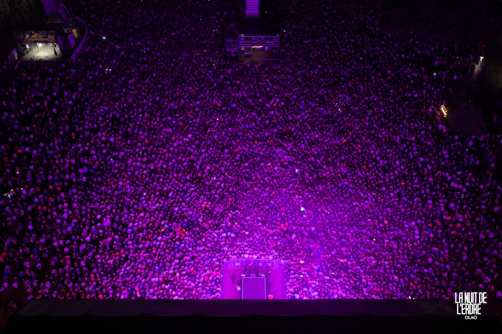 Foule de La Nuit de l'Erdre 2026 vue à la verticale par drone, baignée de lumière violette devant la scène, à Nort-sur-Erdre