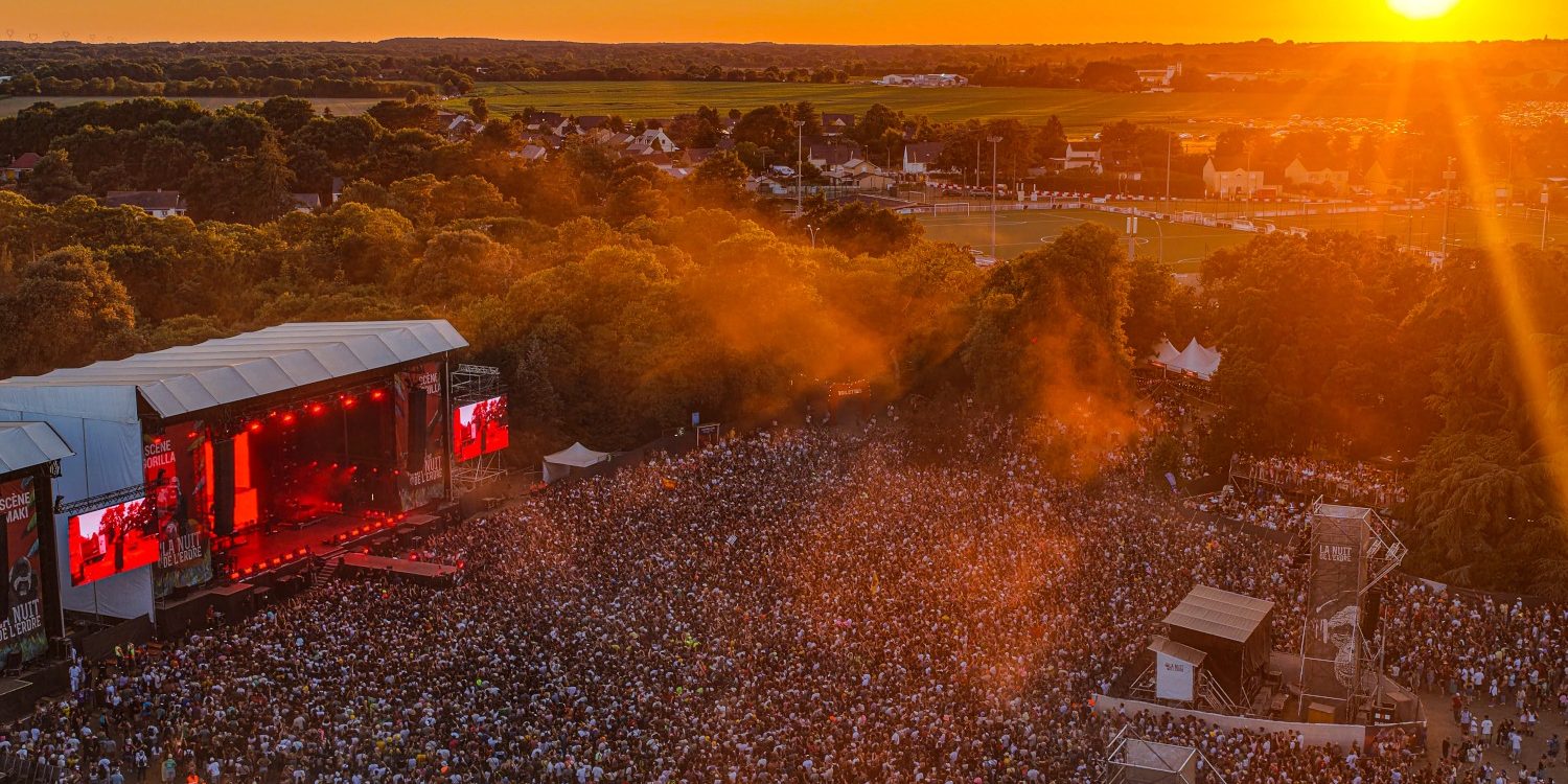 Coucher de soleil sur la grande scène, Nuit de l’Erdre 2026 Coucher de soleil sur la grande scène de La Nuit de l'Erdre 2026, vue par drone au-dessus du public à Nort-sur-Erdre